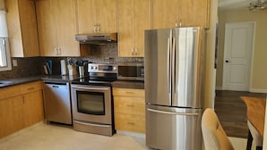 A kitchen with wooden cabinets, stainless steel appliances including a refrigerator, oven, and microwave, and a tiled backsplash.