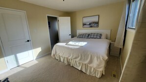 A bedroom with a large bed, a door, a window, and a painting on the wall.