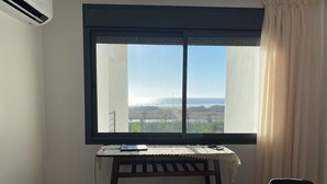 A room with a large window, a small table with a laptop, two chairs, and a bed with a white bedspread. - Bel Appartement Moderne , Vue Océan Front de Mer, Plage, Nature, Détente (Tanger)