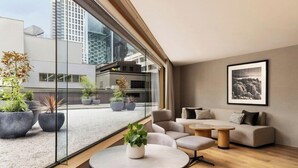 A modern interior with a sofa set, a round table, and potted plants near a large window overlooking a cityscape. - JW Marriott Auckland (Auckland)