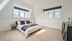 Une chambre à coucher moderne, dotée d’un grand lit, de deux tables de chevet, d’une commode et de deux fenêtres à cadres noirs.