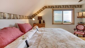 A bedroom with a large bed, a nightstand with a lamp, a window with a view, and a ceiling fan.