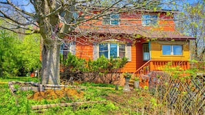 A two-story house with a red and yellow exterior, surrounded by a garden with various plants and a large tree.