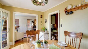 A dining area with a wooden table, chairs, and a chandelier. There is a kitchen in the background with a door leading to another room.
