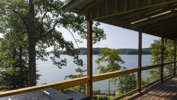 A wooden deck with a grill and a view of a lake.