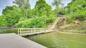 A wooden dock extending into a body of water, surrounded by lush greenery and a small wooden structure on a hillside.