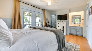 A bedroom with a bed, a ceiling fan, a dresser, a television, and a bathroom visible through an open door.