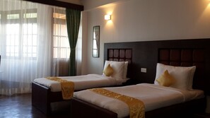 Two single beds with headboards, a bedside table, a wall-mounted light, and a window with sheer curtains. - The Lindsay Himalayan Heights (Gangtok)