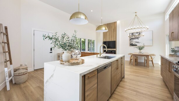 A modern kitchen with a marble island, wooden cabinets, and pendant lighting.