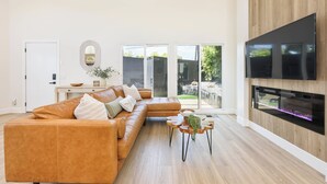 A modern living room with a large sectional sofa, a flat-screen TV mounted on a wooden wall, and a fireplace.