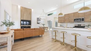 A modern kitchen with wooden cabinets, a central island with stools, and a flat-screen TV mounted above the island.
