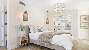 A bedroom with a bed, bedside tables, a mirror, and hanging lights.