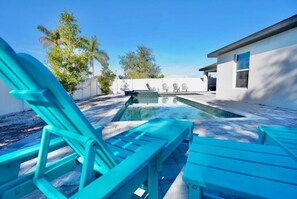 A swimming pool with lounge chairs, a clear sky, and a building in the background.
