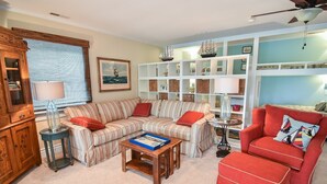 Ein Wohnzimmer mit einem gestreiften Sofa, einem roten Sessel, einer Holzkommode und einem Bücherregal.