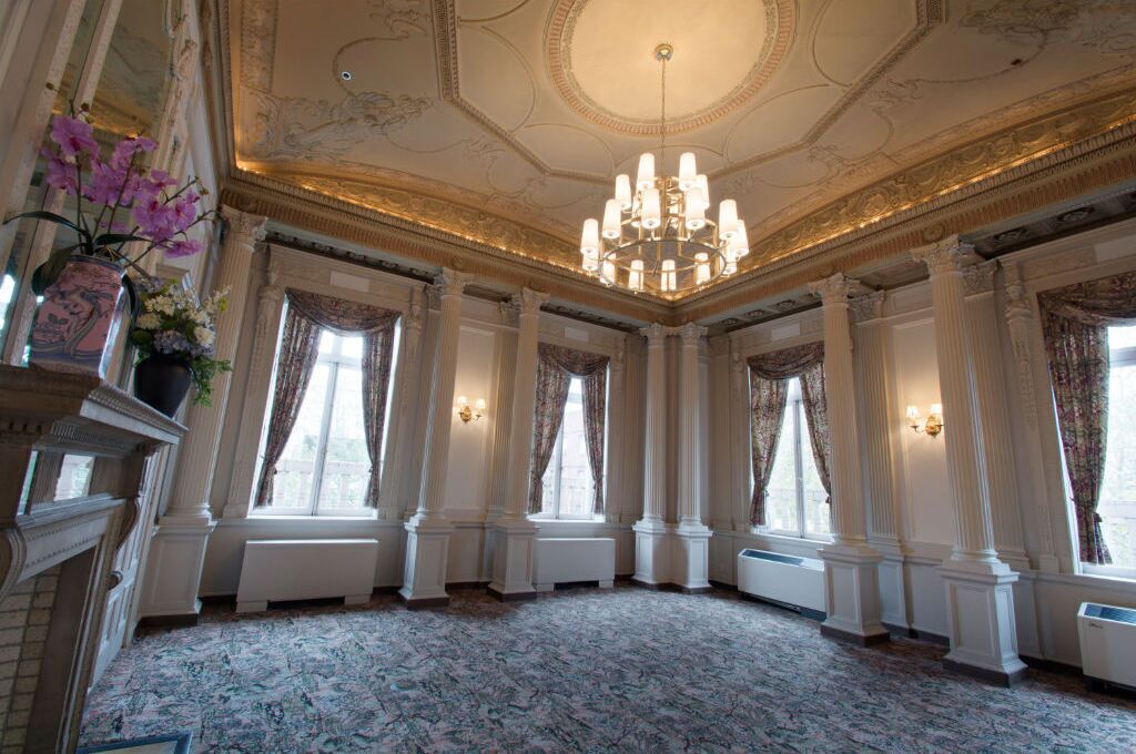 A grand room with ornate columns, a chandelier, and large windows with curtains.