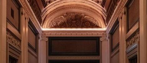 A grand hallway with ornate ceiling details, a reception area, and a polished floor.