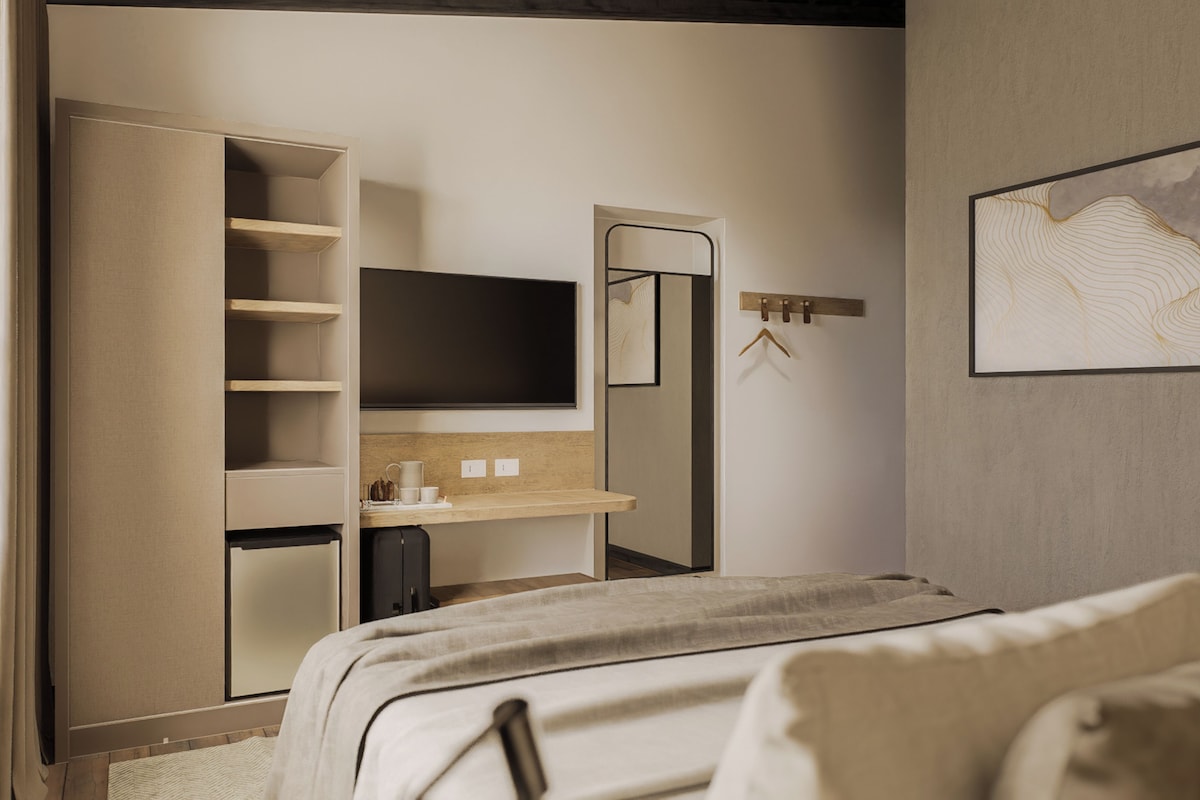A bedroom with a bed, a TV, a wardrobe, a mirror, and a wall-mounted artwork.