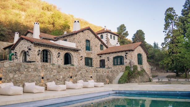 Un edificio de piedra con piscina, mobiliario exterior y un paisaje de colinas al fondo.