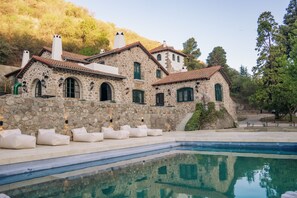 Un bâtiment en pierre doté d’une piscine, d’un espace extérieur aménagé et surplombant une colline.