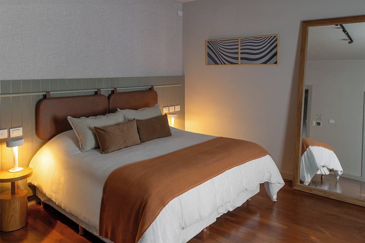 A neatly made bed with a brown headboard, a bedside table with a lamp, and a mirror on the wall.