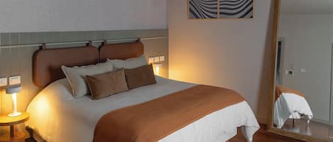 Una cama bien hecha con cabecera marrón, una mesita de noche con lámpara y un espejo en la pared.