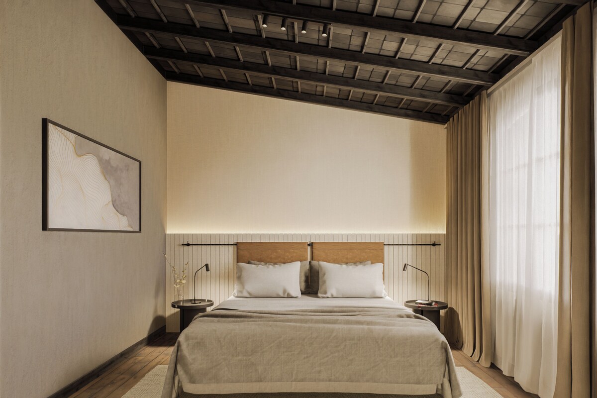 Un dormitorio con una cama grande, cabecera de madera, dos mesitas de noche, una obra de arte enmarcada en la pared y una ventana con cortinas.