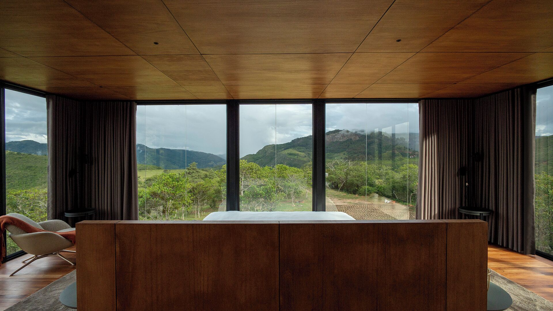 Een modern interieur met een groot houten plafond, een centraal zithoek en ruime ramen met uitzicht op een bergachtig landschap.