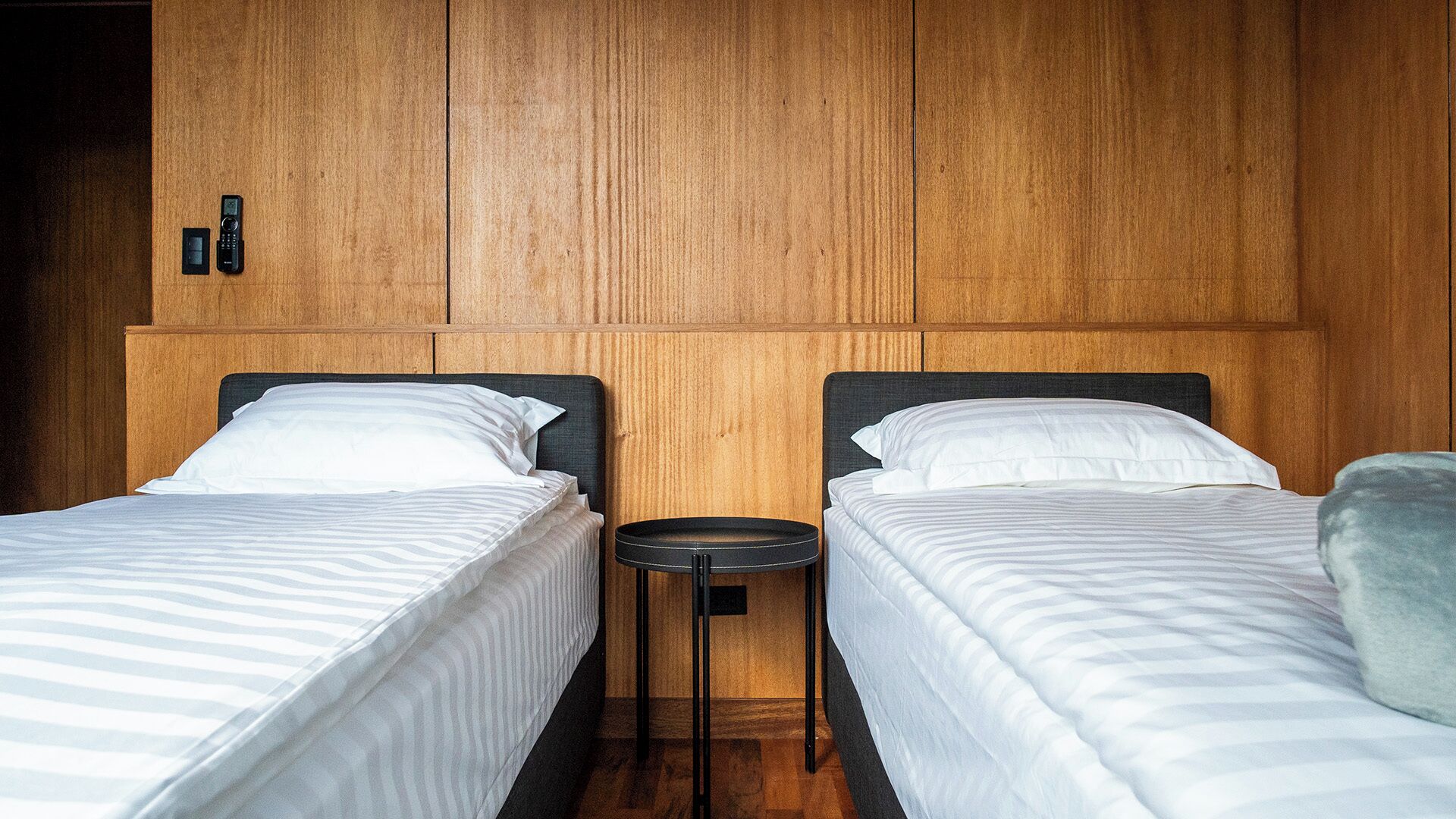 Ein Hotelzimmer mit zwei Einzelbetten, einem kleinen runden Tisch und Holzvertäfelung an den Wänden.