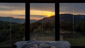 Un dormitorio con un ventanal que da a un paisaje montañoso al atardecer.