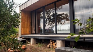 Una casa moderna con ventanas amplias, una terraza de madera y vistas a árboles.