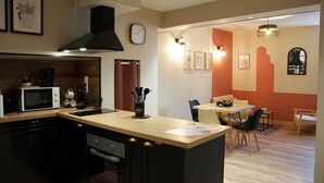 Una cocina compacta con una isla central, un comedor con mesa y sillas, y un reloj visible en la pared.