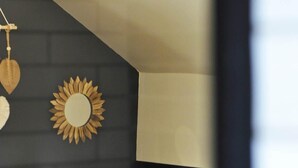 Un dormitorio con cama, almohadas, un espejo adosado a la pared y un adorno con forma de sol.