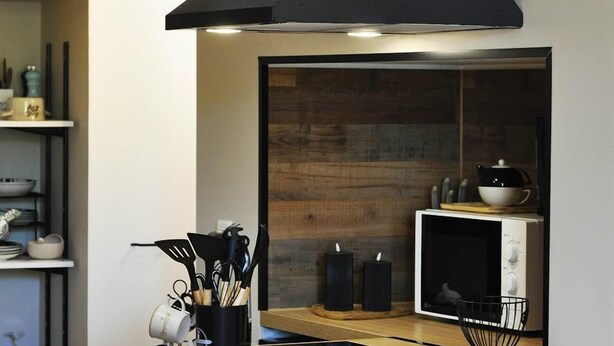 Una cocina moderna con una campana extractora negra, un microondas y una encimera de madera.
