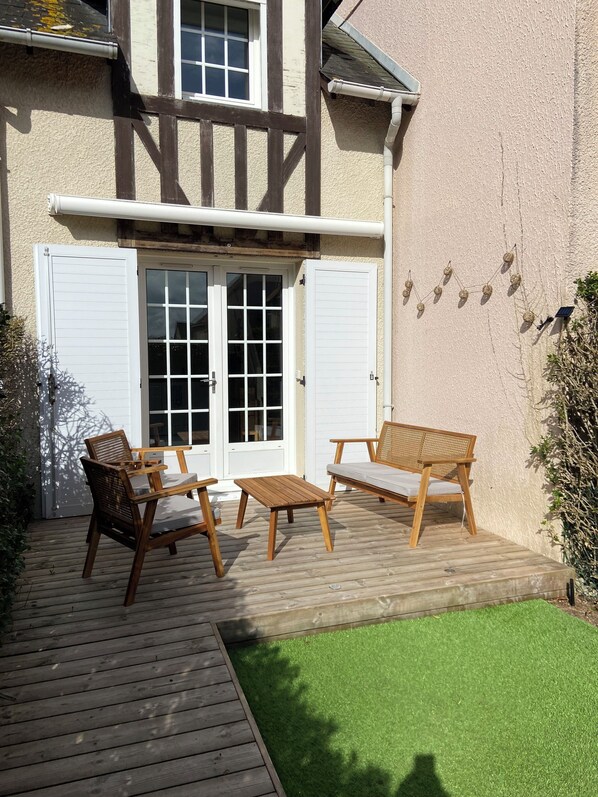 A wooden deck with outdoor furniture, a white door, and a green lawn.