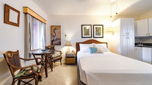 A hotel room with a bed, a desk with chairs, a lamp, and a kitchenette.