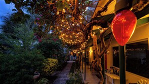 A pathway lined with trees and plants, leading to a building with outdoor seating.
