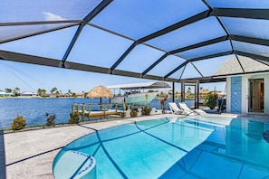 Un espace piscine offrant une vue dégagée sur l’eau, des chaises longues et un coin salon couvert avec un toit de chaume.