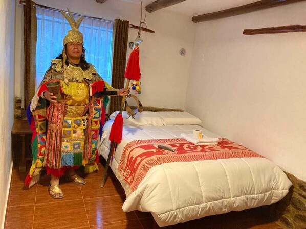 A room with a bed, a person in traditional attire, and a window with curtains. - Mirador Inca (Ollantaytambo)