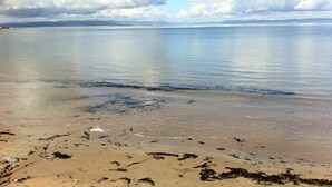 A beach with calm water, distant mountains, and a clear sky.