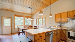 A modern kitchen with wooden cabinets, a large island, stainless steel appliances, and large windows providing natural light.