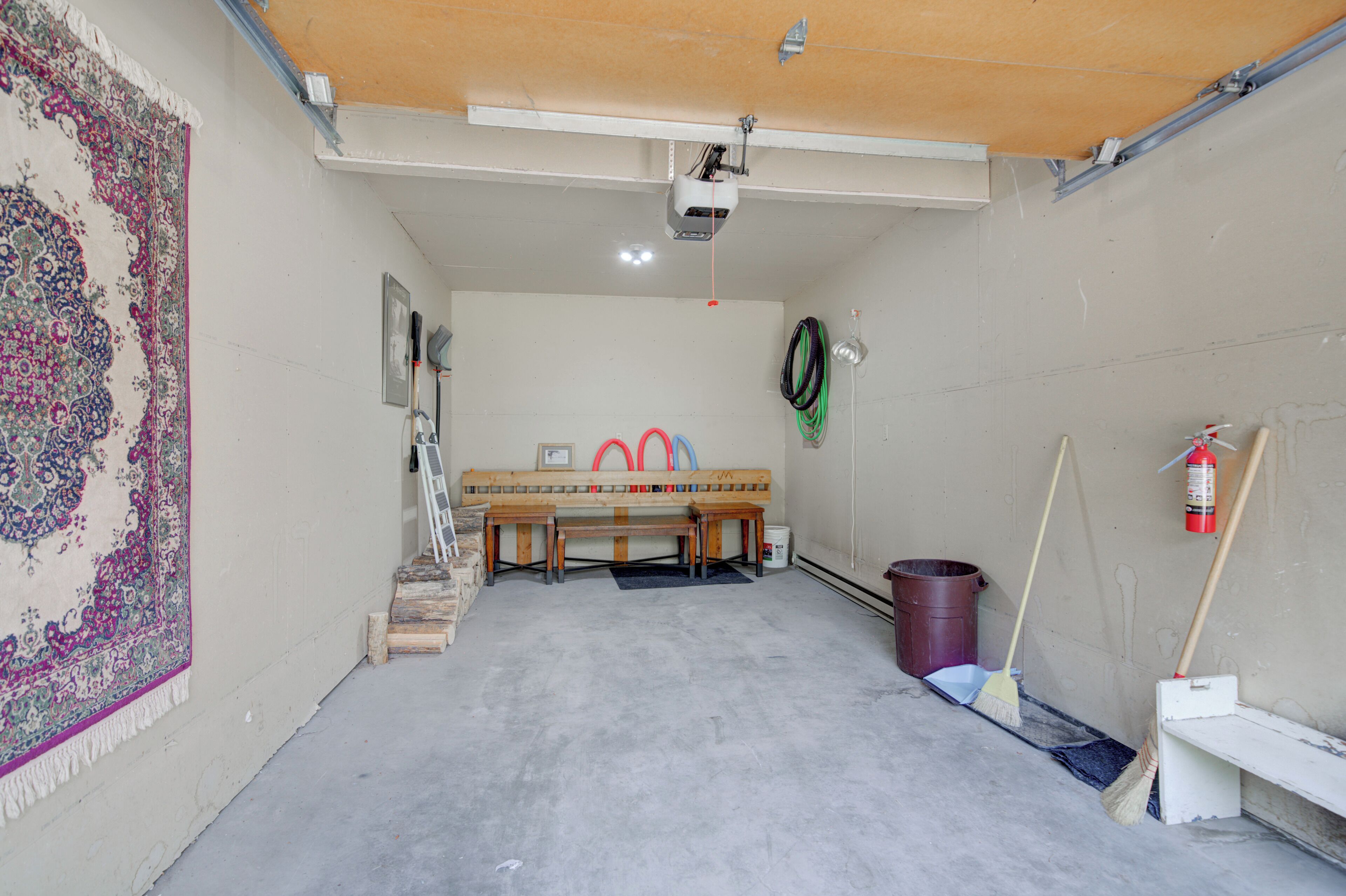 A room with a wooden bench, a fire extinguisher, a broom, and a bucket.