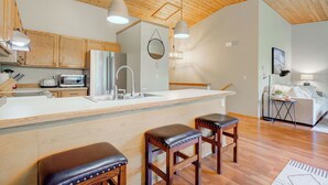 A modern kitchen with wooden cabinets, a large island with stools, a refrigerator, and a microwave.