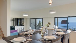 A modern dining area with a large table set for six, featuring a view of the sea through large windows. - Bay Bliss by Atlantic Holiday (Funchal)