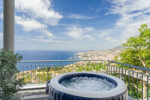 Un jacuzzi en un balcón con vistas a una ciudad costera bajo un cielo despejado.
