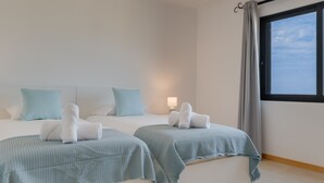 A modern hotel room with two beds, each with a light blue bedspread and white towels. There is a window with a view of the sky and a curtain on the right side. - Bay Bliss by Atlantic Holiday (Funchal)