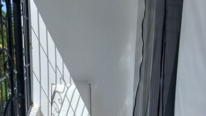 Ein Balkon mit Stuhl, weißen Wänden und einem Fenster mit Vorhang.