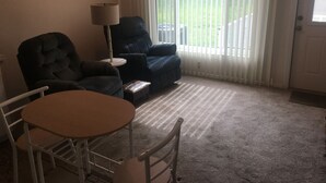 Una sala de estar con un sillón azul oscuro, una silla más pequeña, una mesa redonda y una lámpara.
