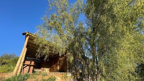 A rustic wooden cabin with a sloped roof, surrounded by dense greenery and trees.
