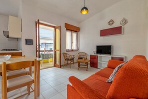 Un salon avec un canapé, une table à manger avec des chaises, un téléviseur et un coin cuisine équipé d’une cuisinière.