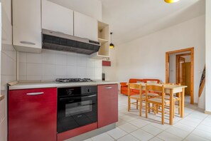 Uma cozinha com fogão, forno e armários vermelhos. Há uma mesa de jantar com cadeiras e um sofá vermelho ao fundo.